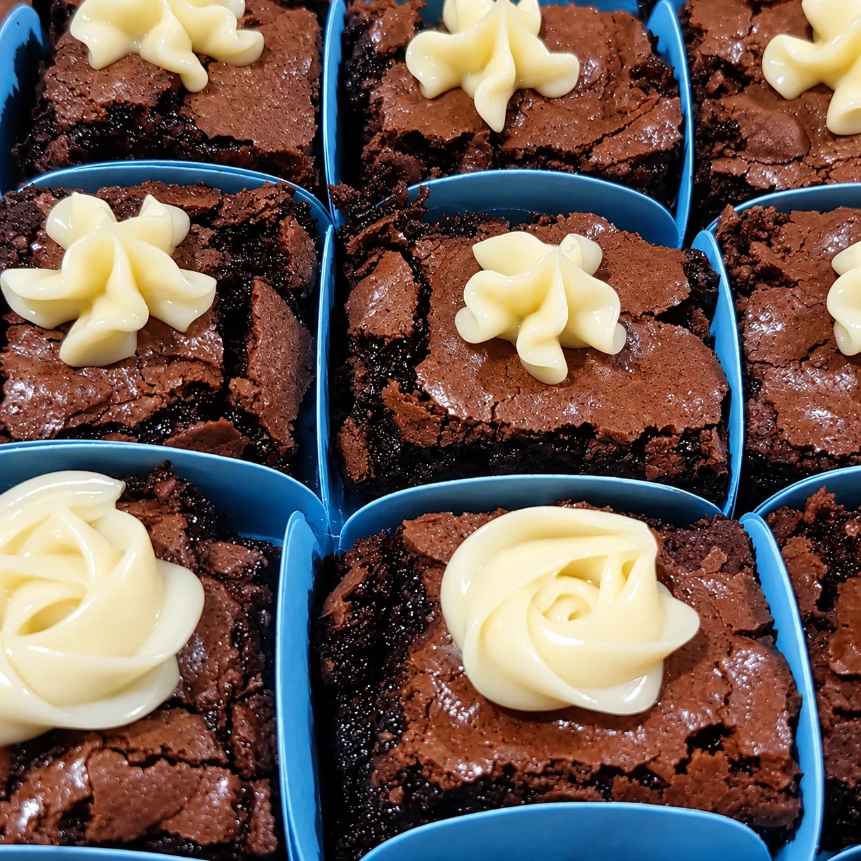 Brownies em forminhas azuis, cada um com um confeito de creme branco por cima